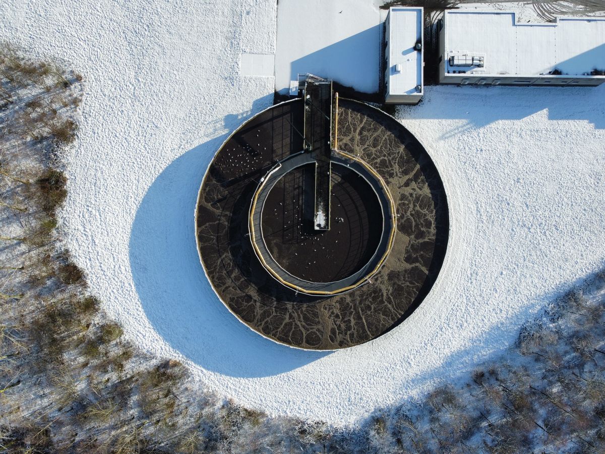 Round clarifier at a wastewater treatment plant seen from above in snow, where solids settle out of sewage before the treated water is discharged