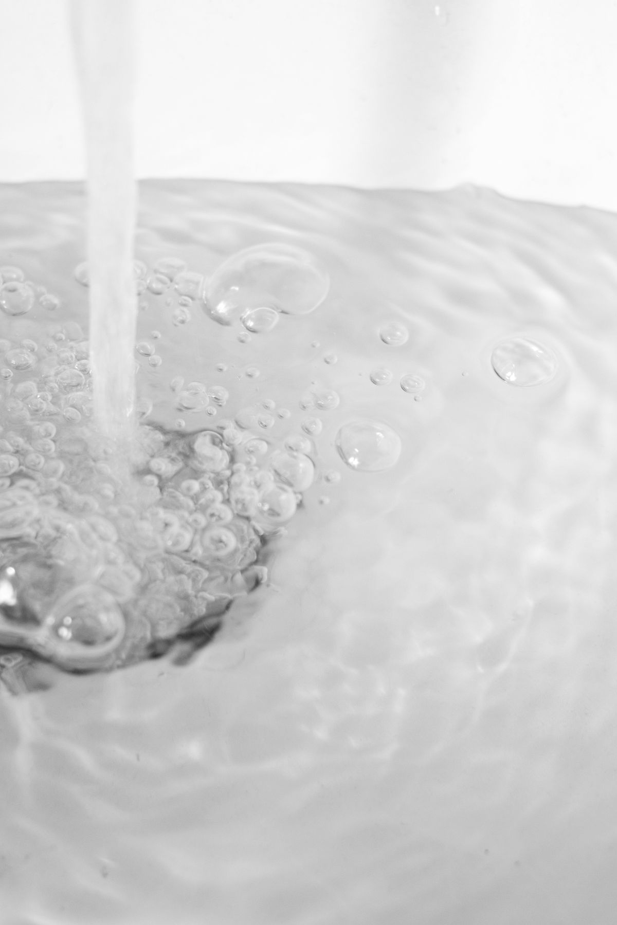 Water flowing steadily from a tap into a sink with bubbles on the surface, the same uninterrupted flow a stuck brine valve sends into a softener tank