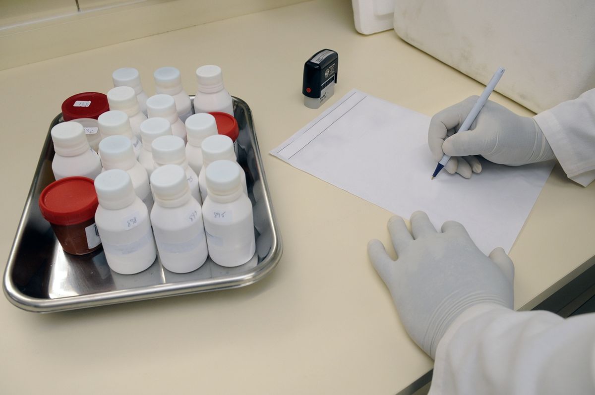 Laboratory technician writing up results beside sample bottles in a lab, the record behind a published certification listing