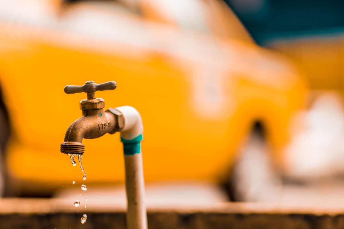 Close-up of water droplets on a brass faucet against a yellow background, representing the intermittent air-and-water spurts that follow a softener regeneration fault