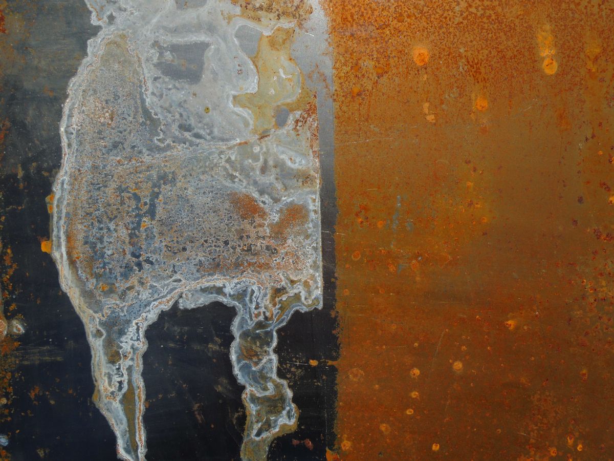 Corroded sheet metal showing orange rust staining across its surface, the same iron oxide film that coats resin beads on untreated well water