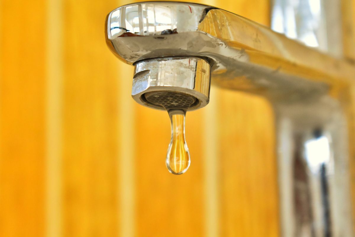 Close-up of a water droplet hanging from the end of a stainless steel faucet, the kind of tap where partly hard water from a leaking bypass shows up without any visible sign