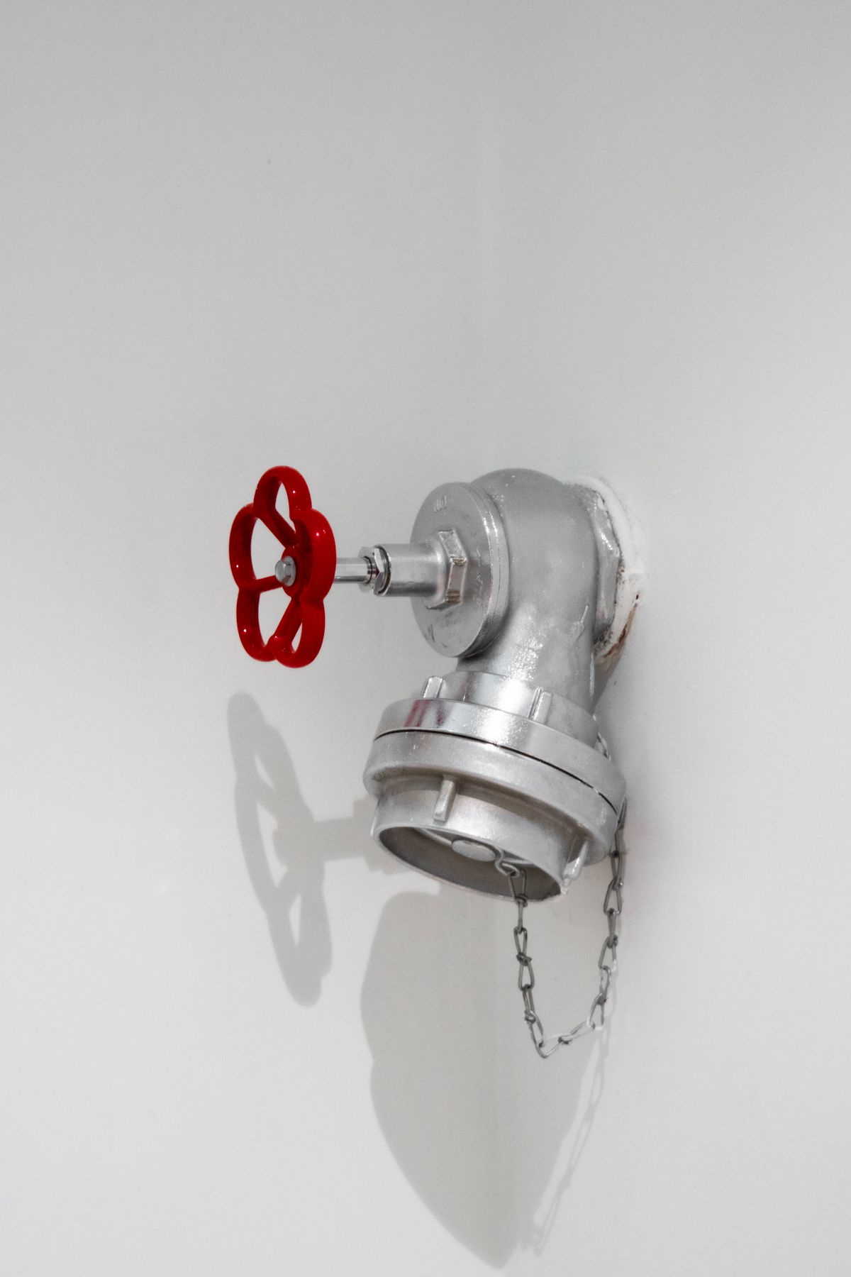 Silver plumbing pipework with a red shut-off valve mounted on a white wall, the kind of supply connection where a water hammer arrestor should be fitted close to the closing valve