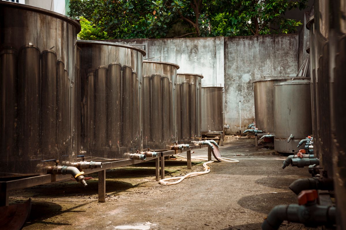 Row of large industrial metal pressure tanks joined by pipework, the same vessel-and-riser design scaled down inside a household water softener mineral tank