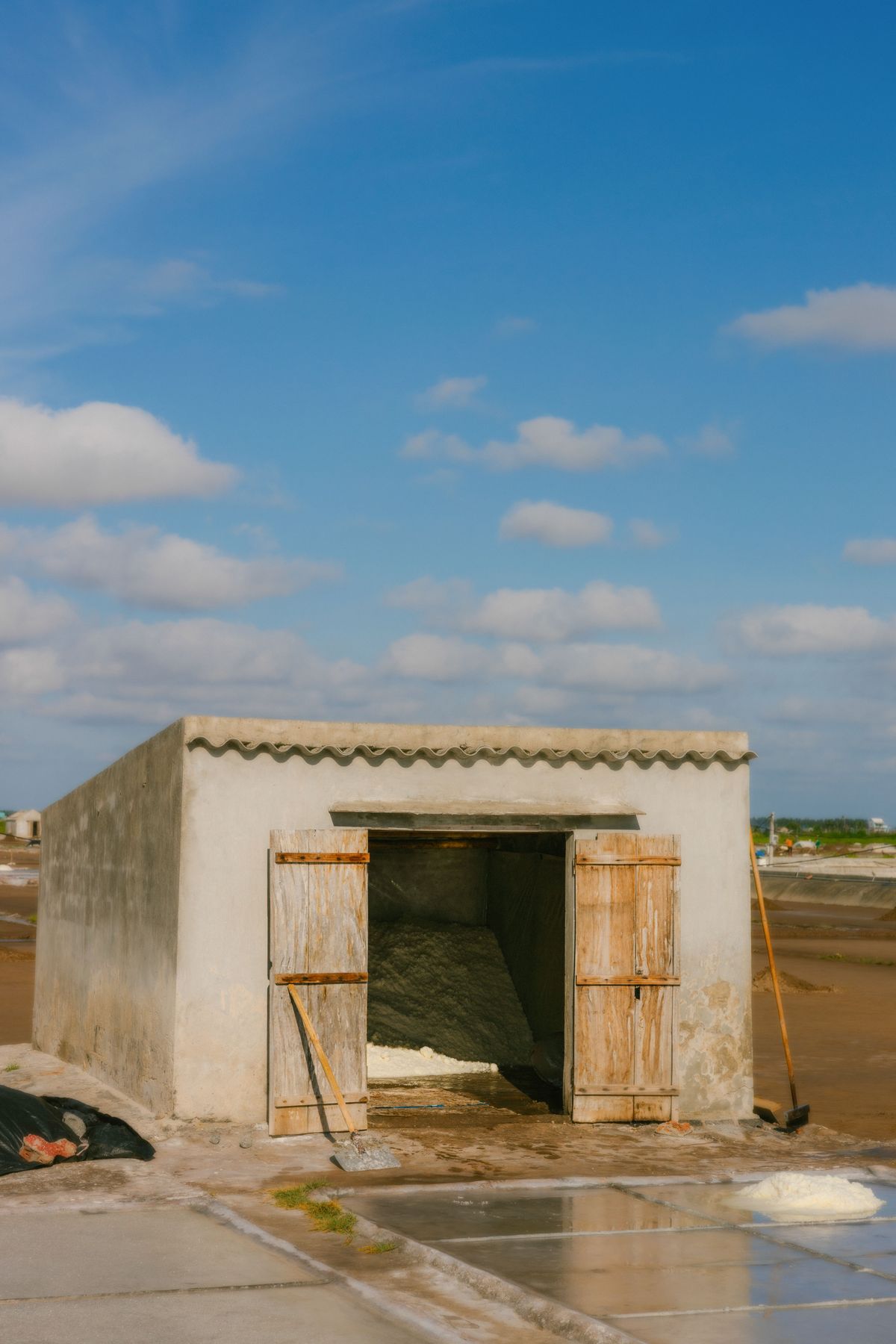 Small concrete storage shed at a salt works with its wooden doors open on a dry pile of harvested salt