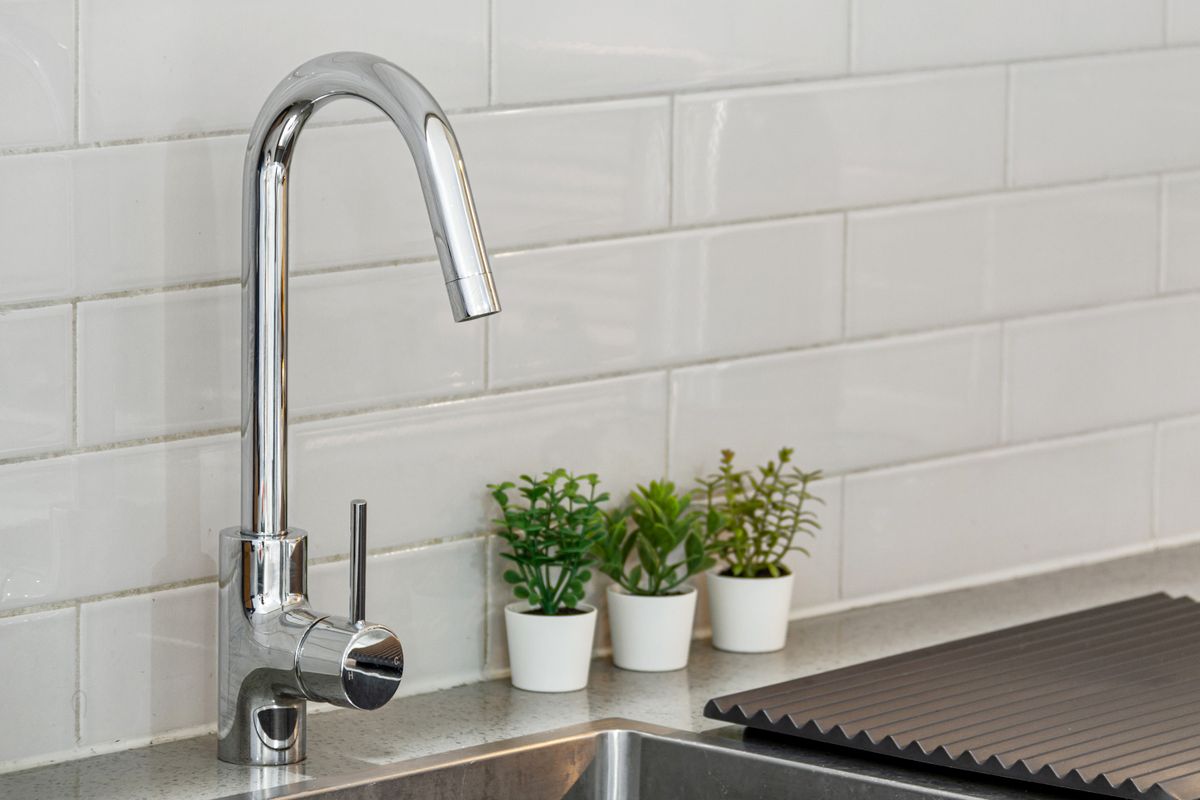 Modern stainless steel kitchen sink and chrome faucet under a white tiled backsplash, where city water with a chlorine residual reaches a softened home