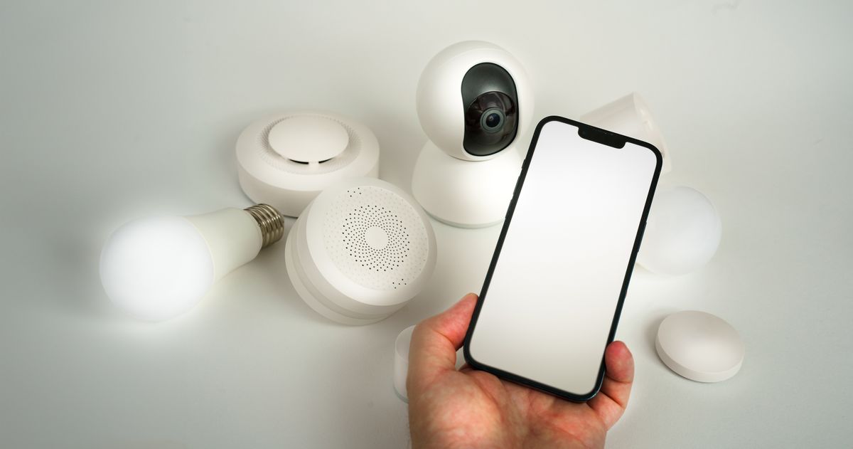 Hand holding a smartphone among white smart home sensors, a camera and a smart bulb, the app-connected devices that now carry a smart water softener's leak and flow features