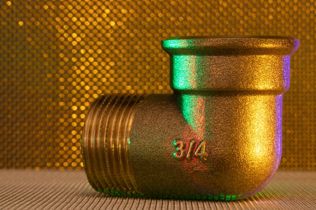 Brass pipe fitting photographed against a warm background, the plumbing metal most often responsible for a metallic taste