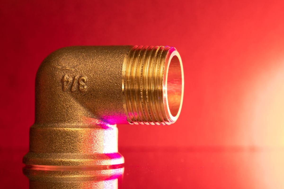 Brass pipe elbow fitting against a red background, representing the closed plumbing fittings in which heated water has nowhere to expand