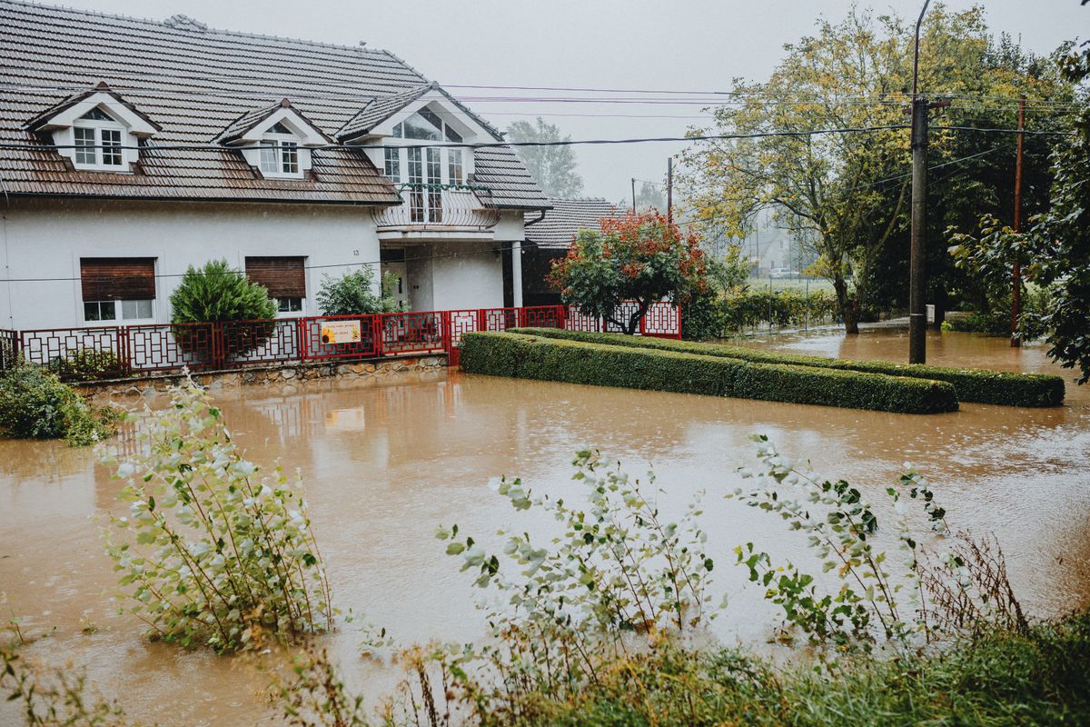 Suburban house with brown floodwater spreading across the garden after heavy rain, the kind of event that leaves a basement water softener standing in contaminated water