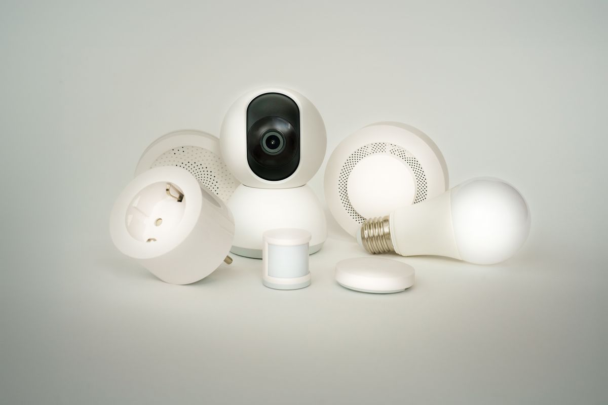 Collection of white smart home devices including wireless sensors, a smart plug and a camera, all controlled from a phone app