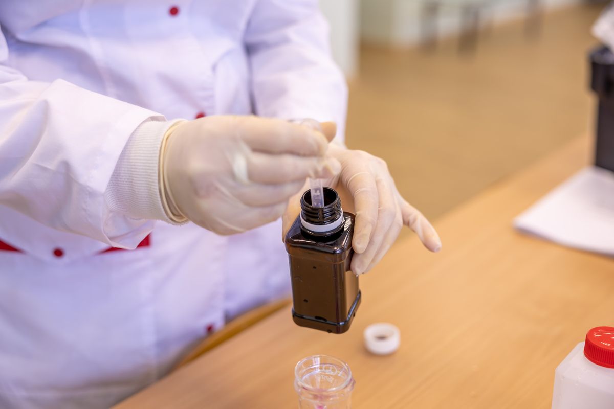 Gloved lab technician drawing a sample from a brown sample bottle for analysis on a laboratory bench