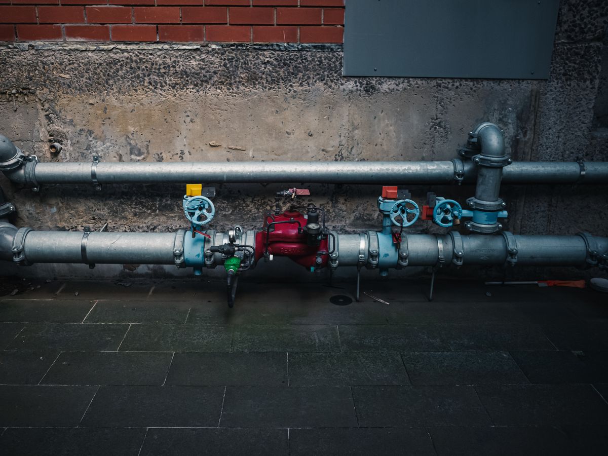 Painted industrial pipework and coloured isolation valves on a wall, the downstream plumbing a passing outlet test says nothing about