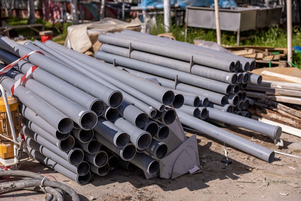 Stack of gray PVC drain pipe lengths at a job site, the rigid pipe often used when a water softener drain line run is long or climbs overhead