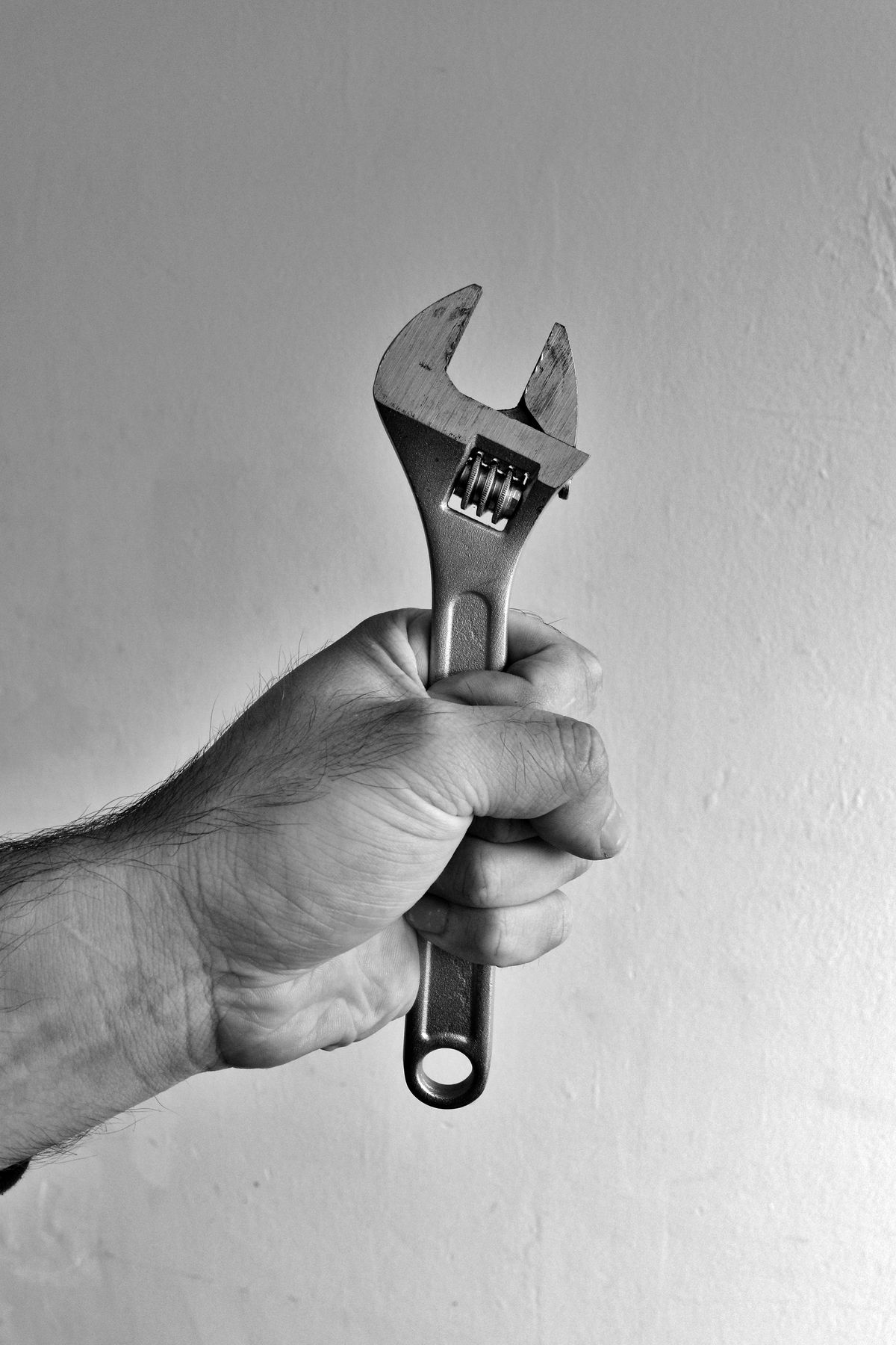 Close-up of a hand gripping an adjustable wrench, the kind of simple tool that covers most owner-level softener repairs