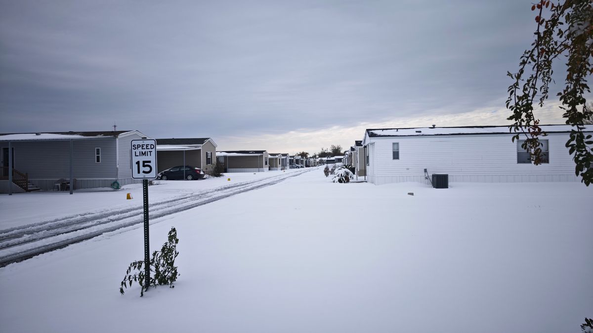 Row of manufactured homes in a mobile home park after heavy snow, with a snow-covered street and a speed limit sign