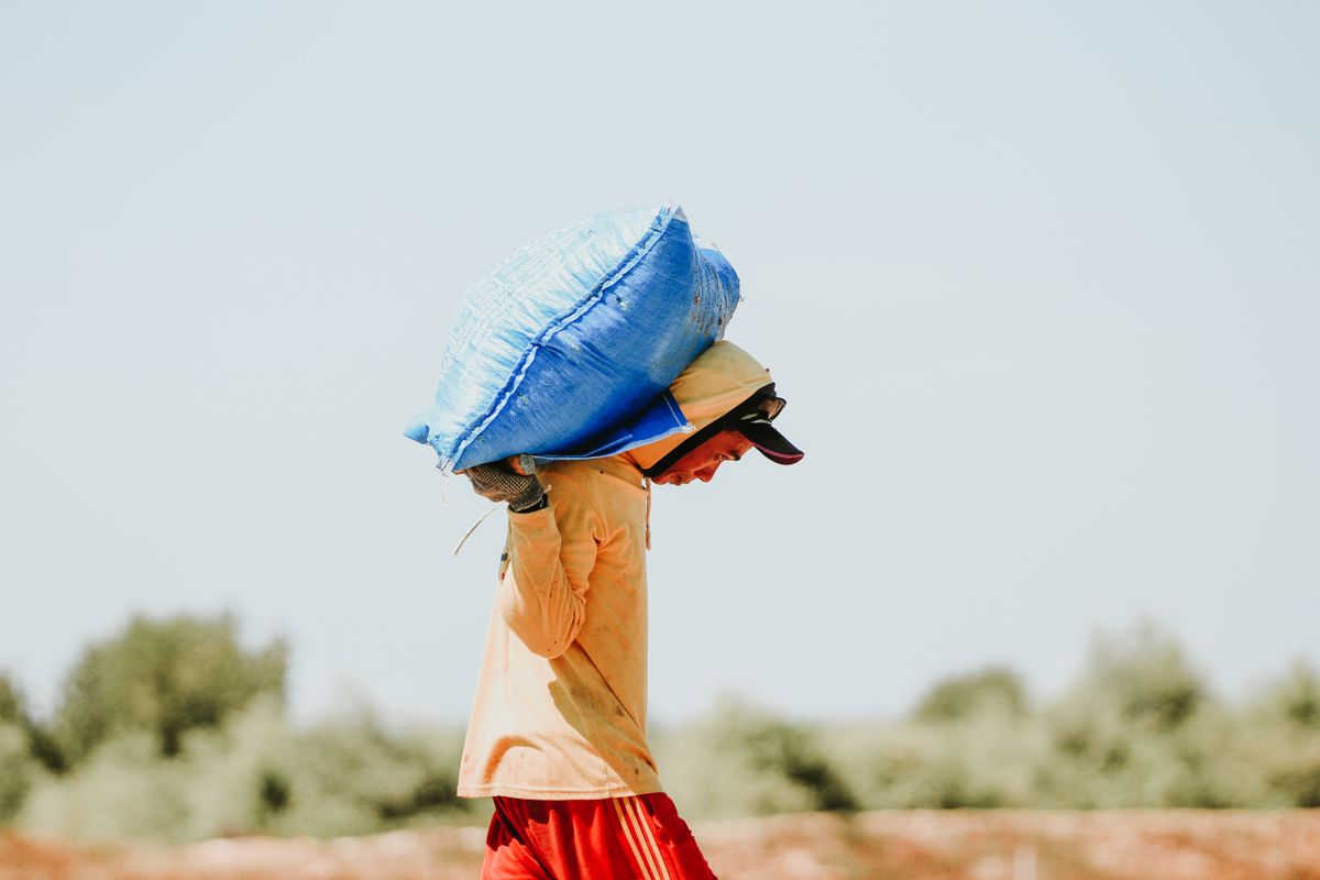 Worker carrying a heavy sack of white salt across a salt field, the yearly salt load a Morton water softener promises to reduce