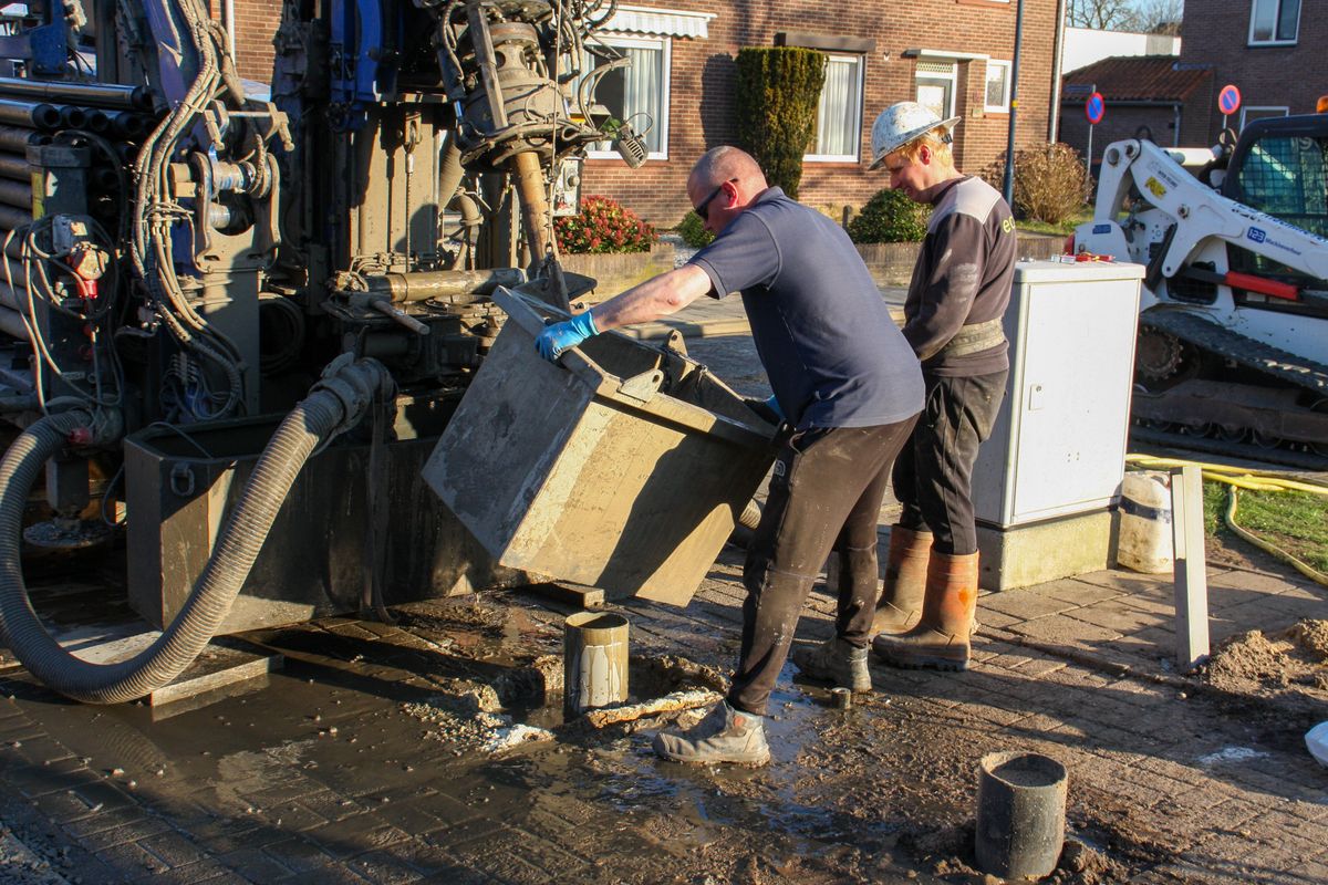 Drilling crew handling equipment and drilling fluid at a rig beside a residential street; drilling and repair work can carry iron bacteria into a well