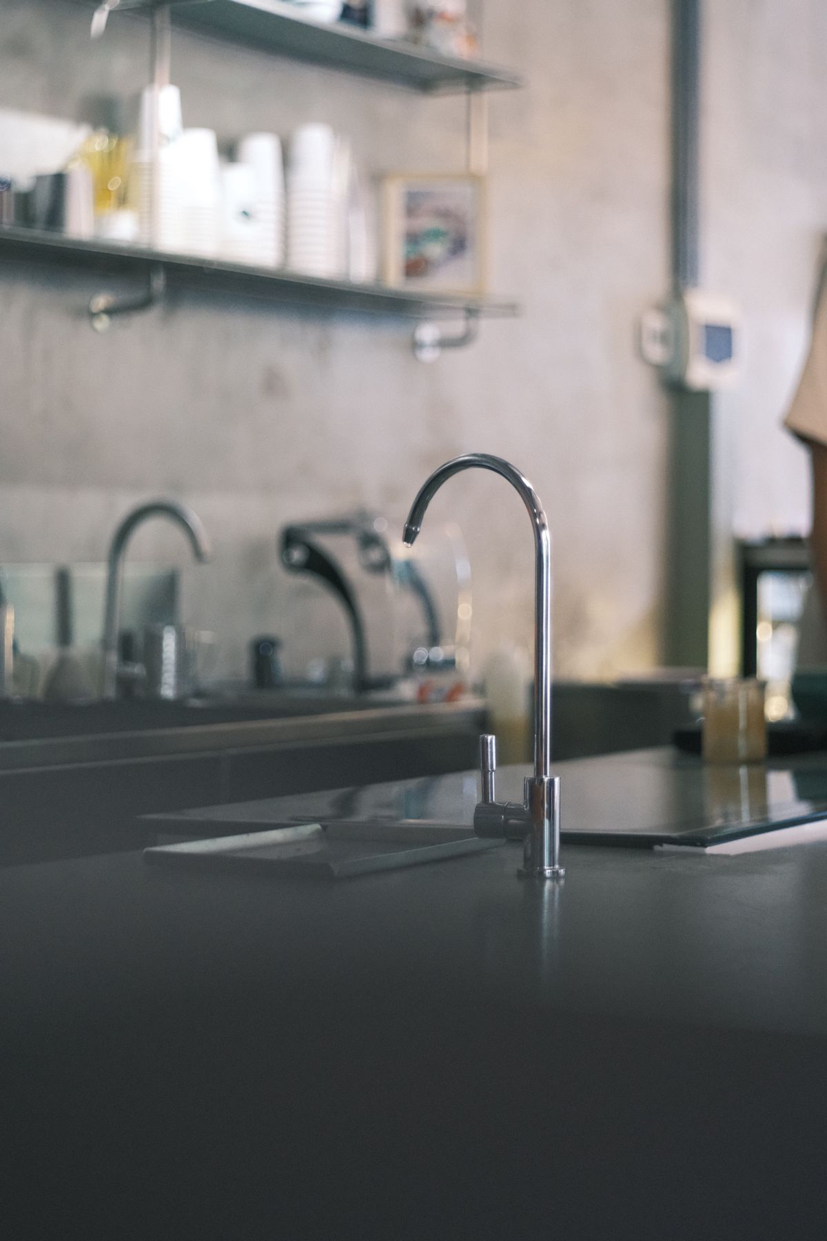 Modern kitchen with a tall chrome gooseneck faucet over a dark countertop, a kitchen sink setup where an under-sink tankless RO system and its faucet are fitted