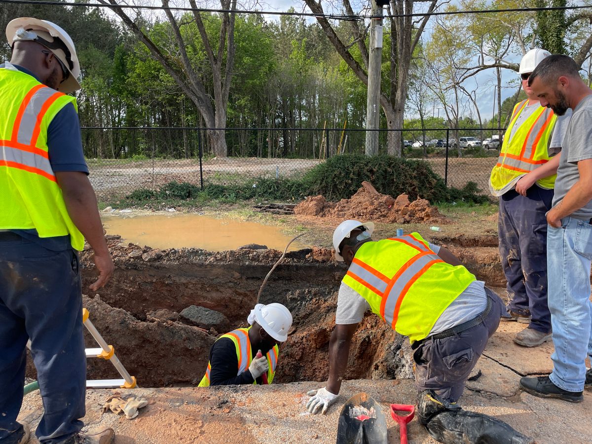 Utility crew in hard hats and safety vests repairing a buried water pipe in a flooded trench after a water main break