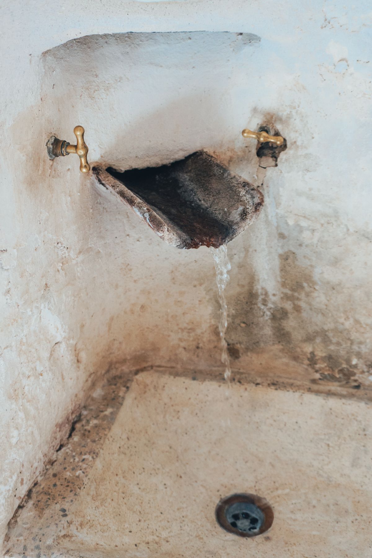 Old tap dripping into a stone basin with heavy mineral deposits, a fixture fed by a line that bypassed treatment