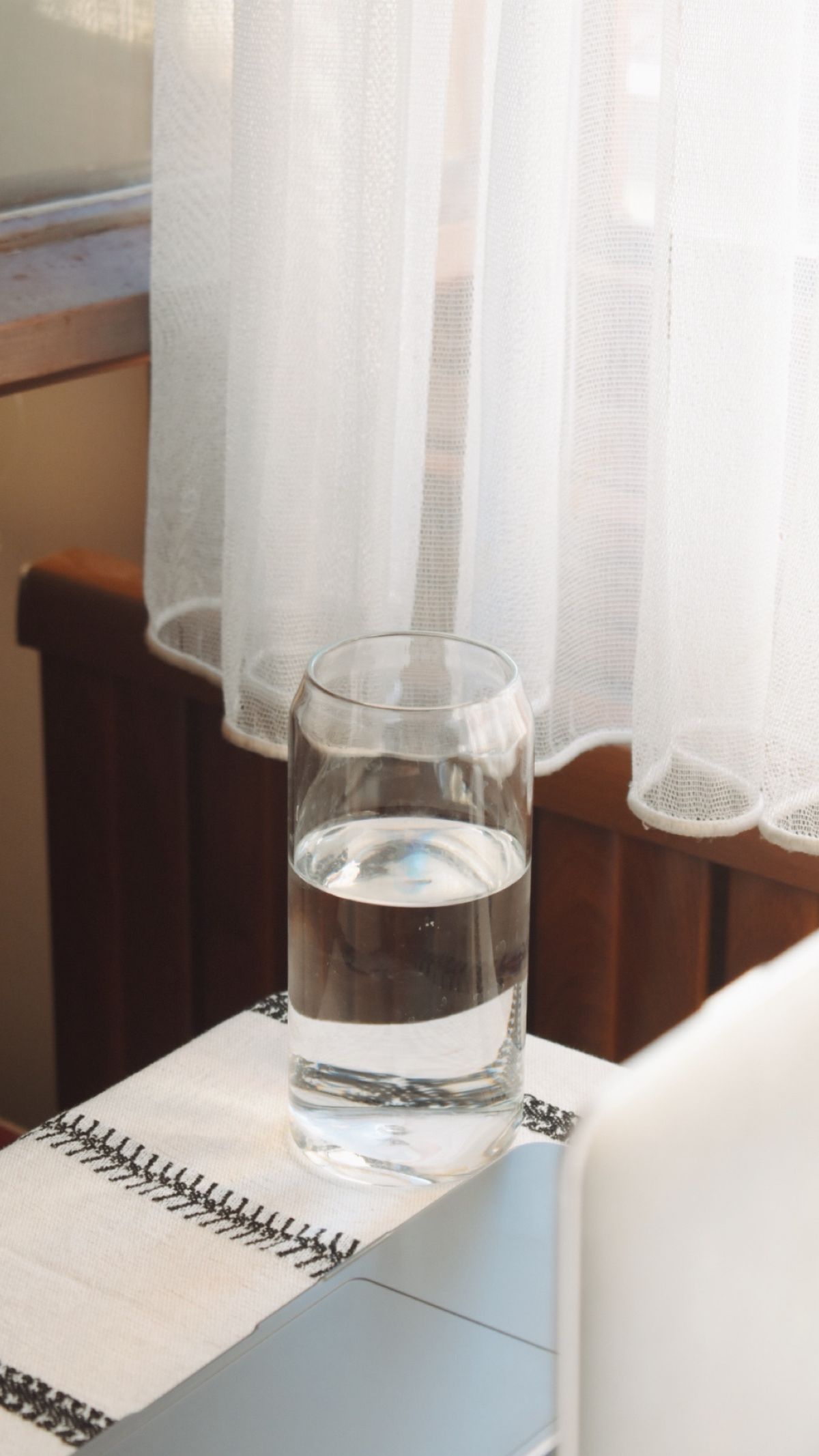 Clear glass of drinking water on a table beside a window with sheer curtains, the purified water a countertop RO purifier dispenses