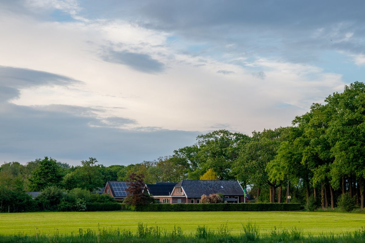 Rural brick house with solar panels behind a wide green field and tall trees, a property beyond the sewer line where softener regeneration water goes to a septic tank