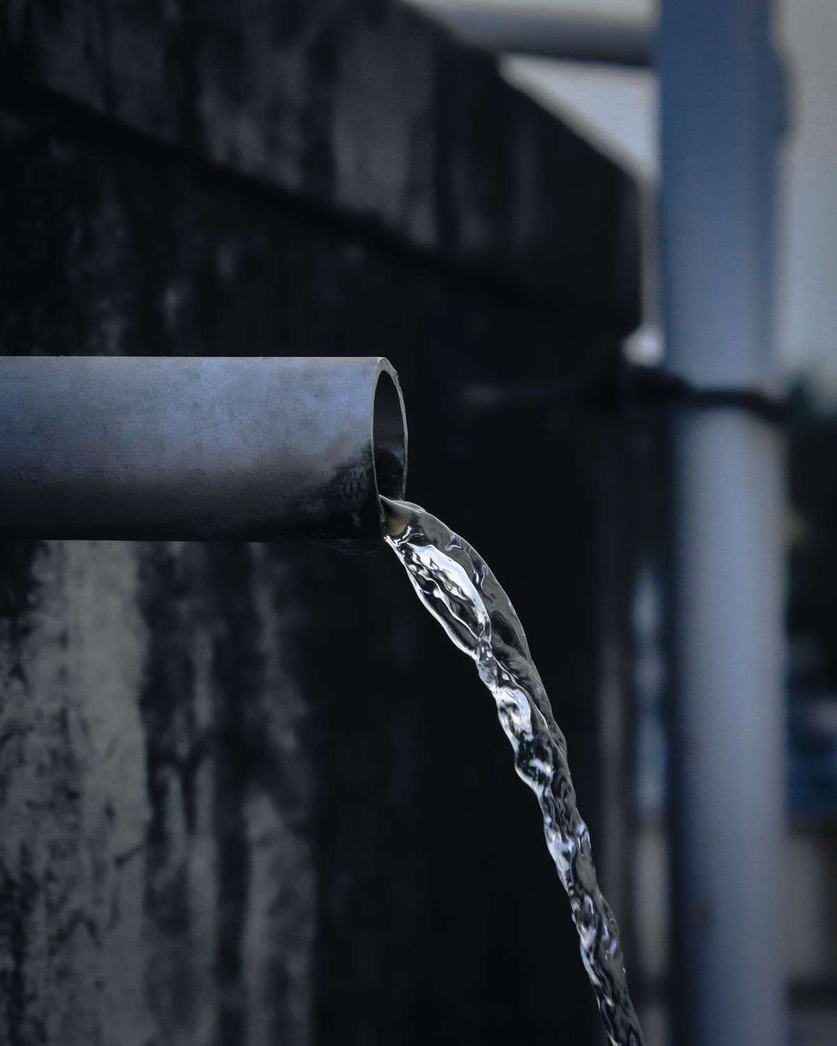 Water discharging steadily from an industrial metal pipe outdoors, comparable to the drain flow during the brine draw and rinse stages of a regeneration
