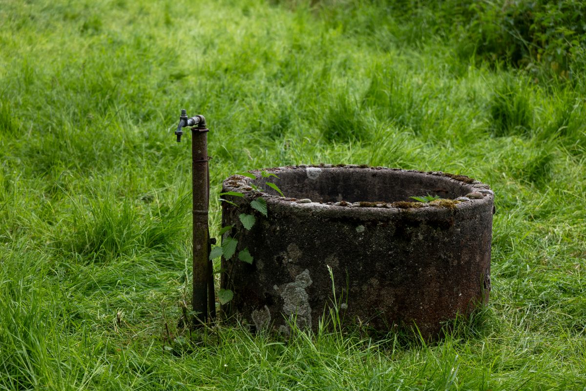 Old stone well with a metal standpipe tap in a grassy field, a private well water supply of the type iron softeners treat