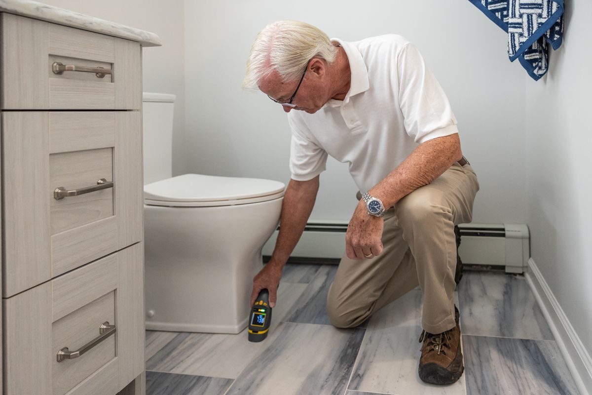 Home inspector kneeling on a bathroom floor and taking a reading with a handheld meter during a house inspection