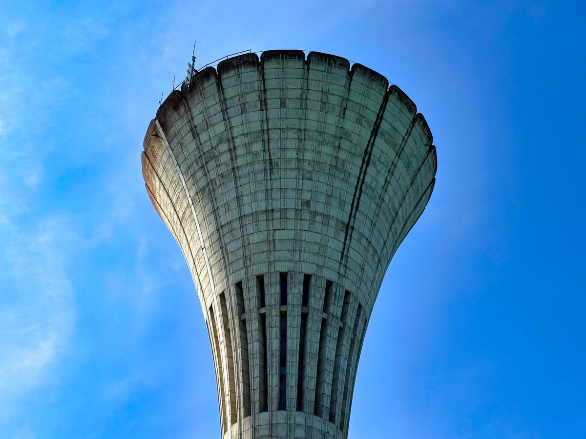 Concrete municipal water tower against a clear blue sky, part of the city distribution system that carries a chlorine residual to household taps