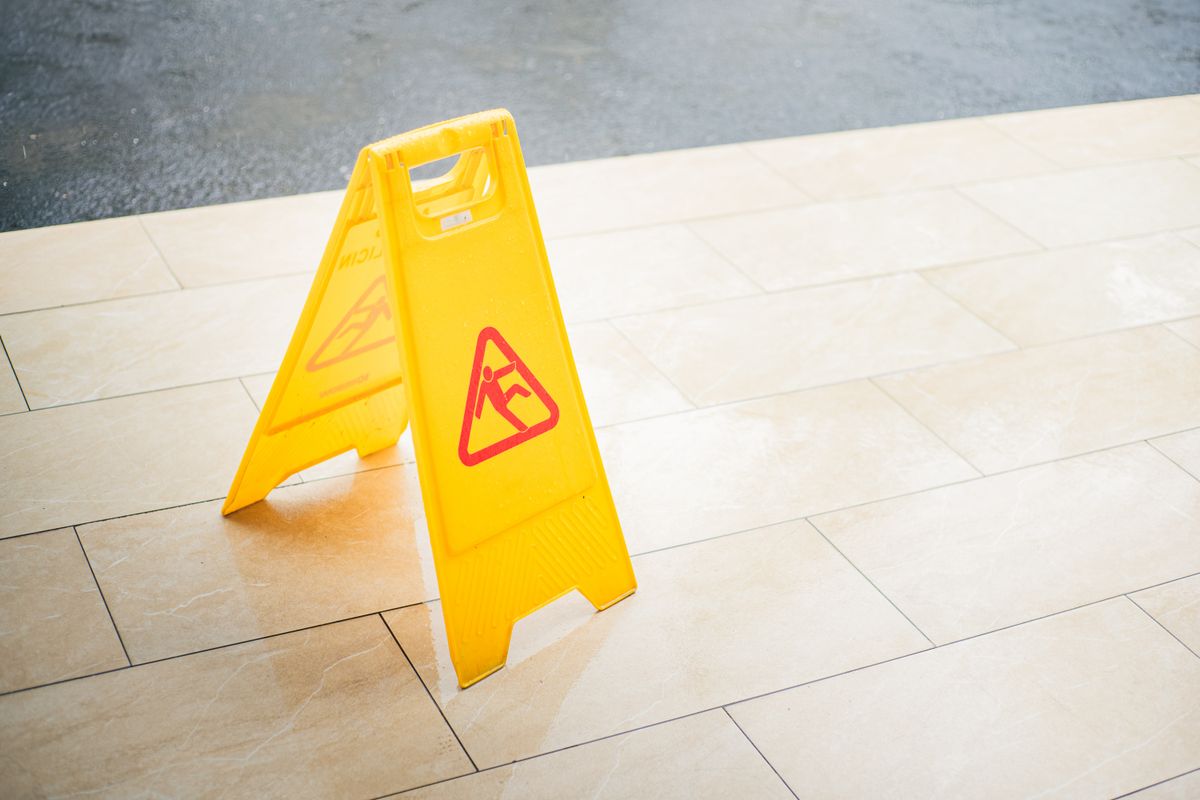 Yellow wet floor caution sign standing on a tiled floor, warning of water on the floor