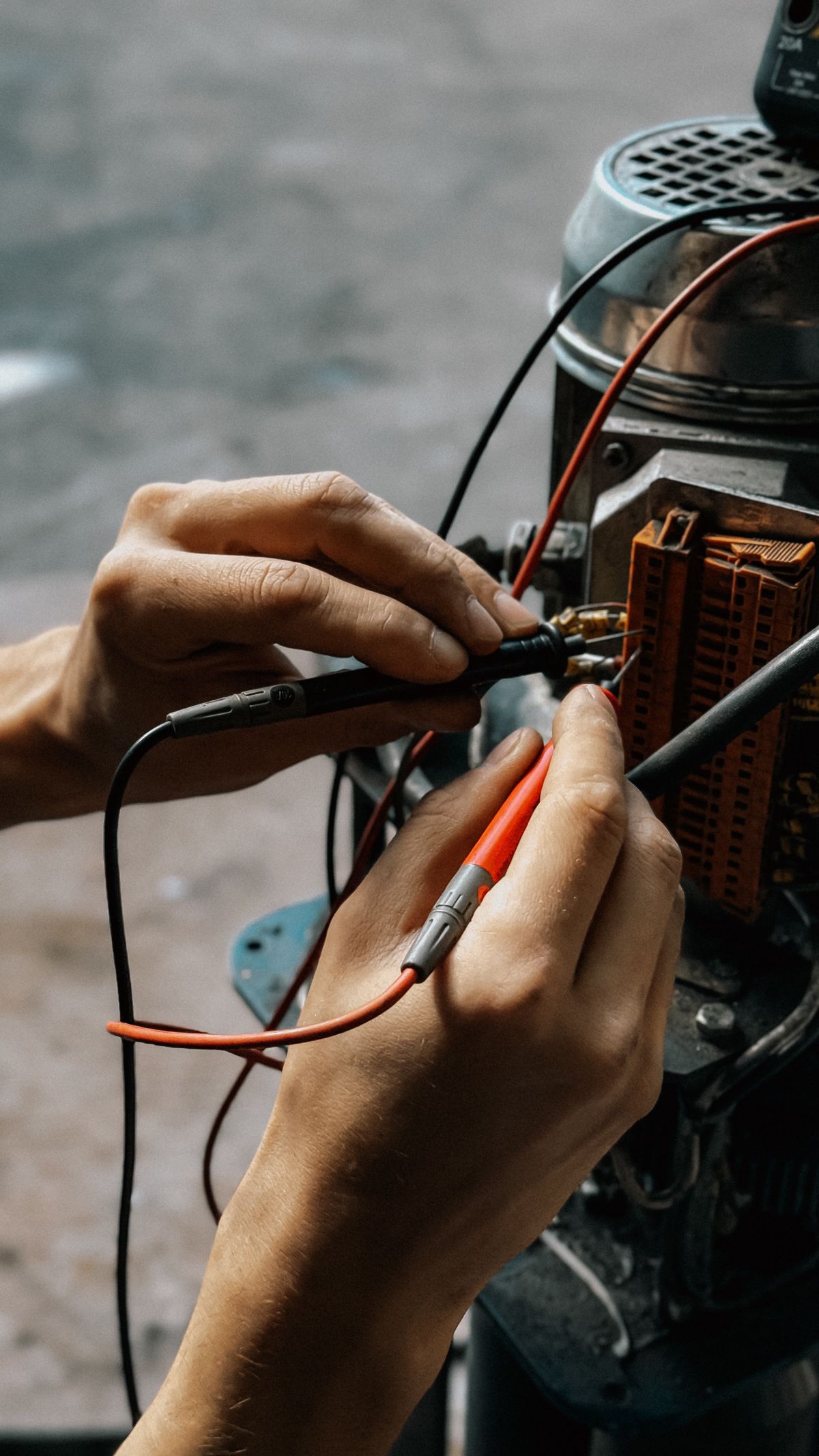 Hands holding red and black meter probes against the wiring terminals of a small electric motor, the drive motor being the first suspect when a softener valve stops advancing