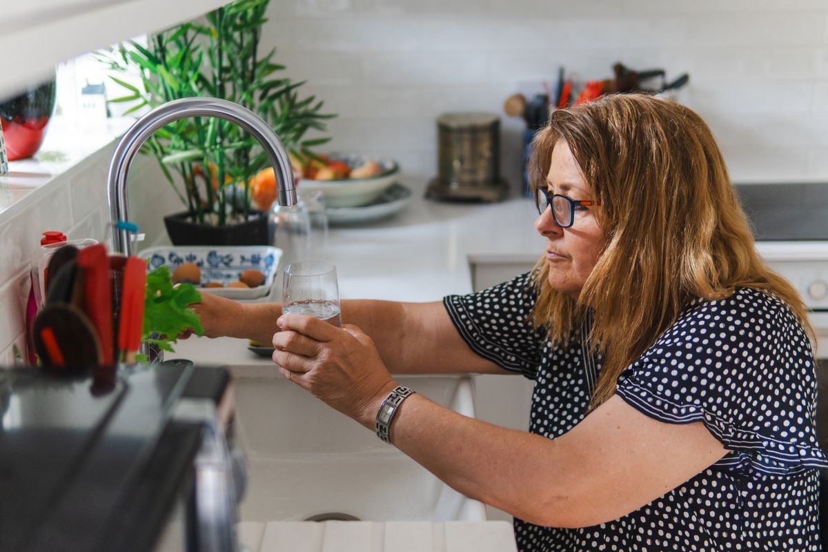 Woman filling a glass at her kitchen tap, drawing a cold water sample to compare against a utility hardness report