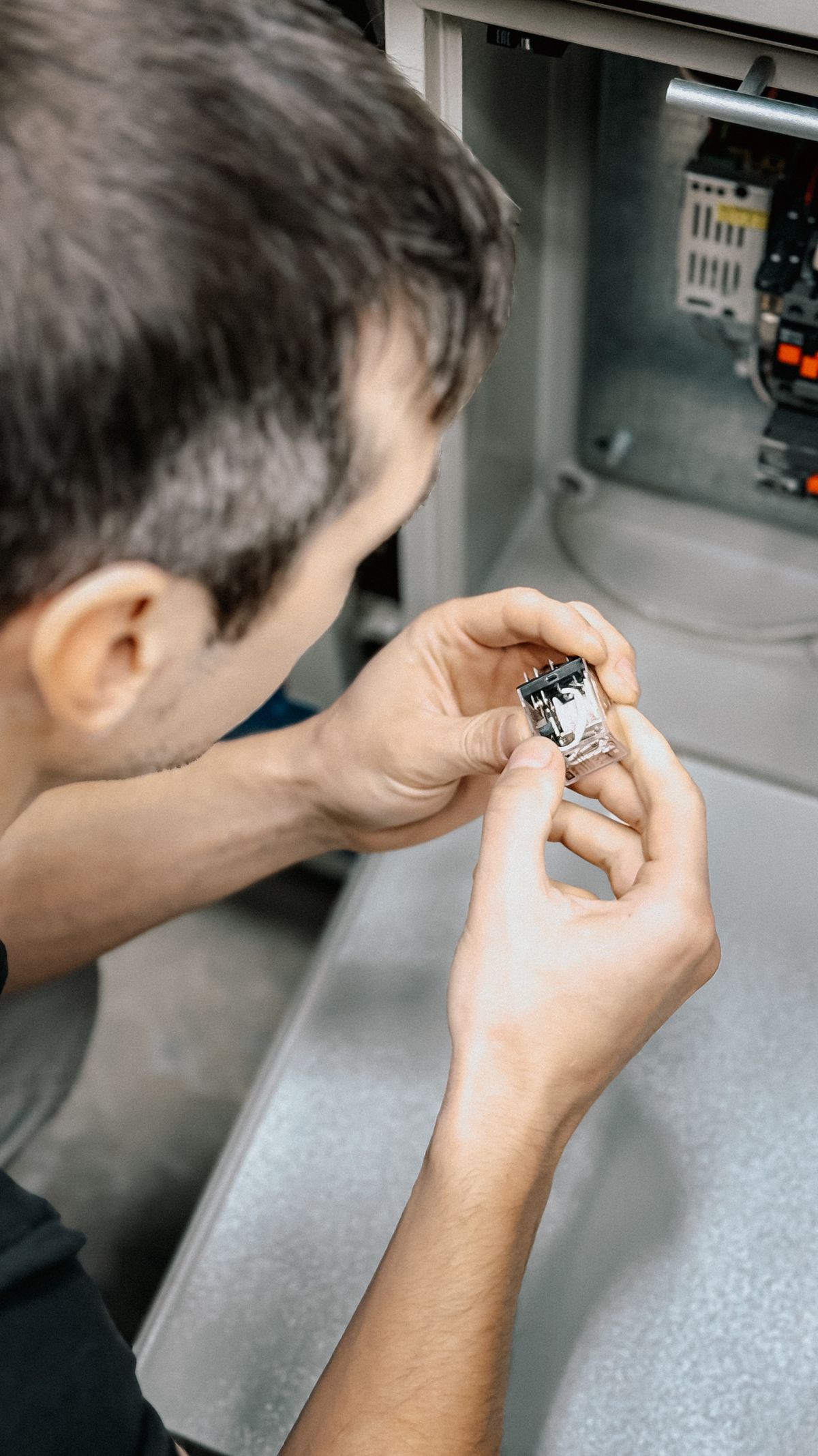 Technician holding a small relay switch up to the light in front of an open control cabinet, the kind of close component inspection that isolates why a softener valve has stopped mid-cycle