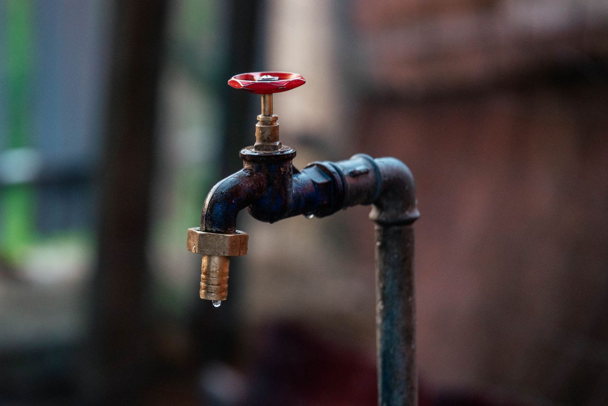Rusty outdoor faucet with a single water droplet falling, the kind of low hose bib that is opened first when purging air from the plumbing