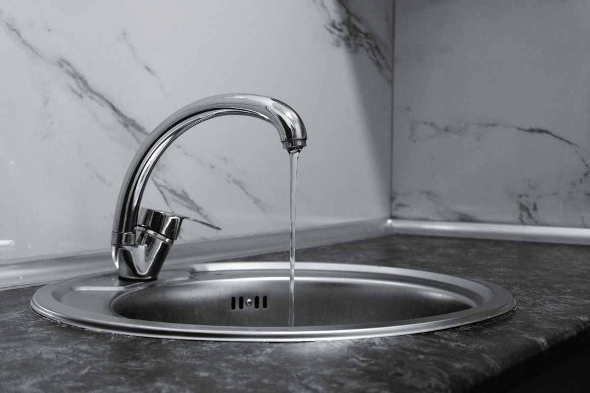 Chrome kitchen faucet running water into a round steel sink, the tap most often plumbed to bypass the water softener