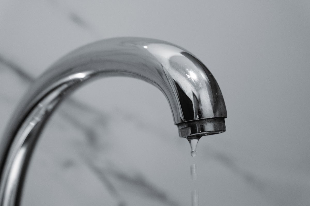 Chrome bathroom faucet with water dripping from its tip, the kind of spitting, interrupted flow that trapped air produces after softener service