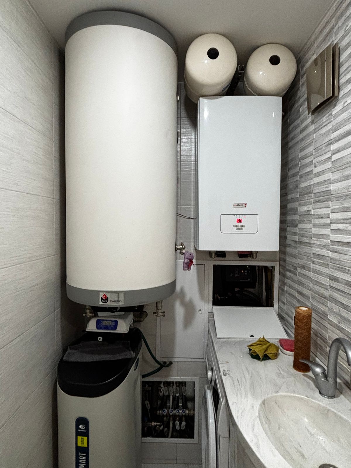 Wall-mounted white hot water storage cylinder in a utility closet with a cabinet water softener installed directly below it