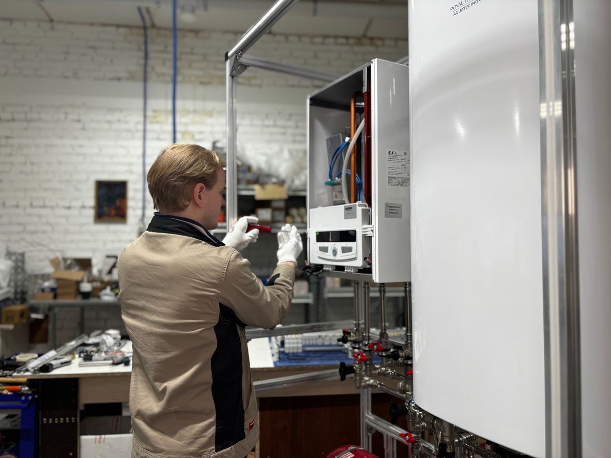 Technician inspecting and servicing a wall-mounted heating unit in a workshop