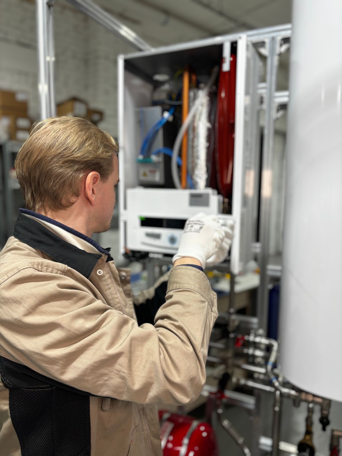 Technician in white gloves adjusting the control panel of an open wall-mounted water heating unit during service