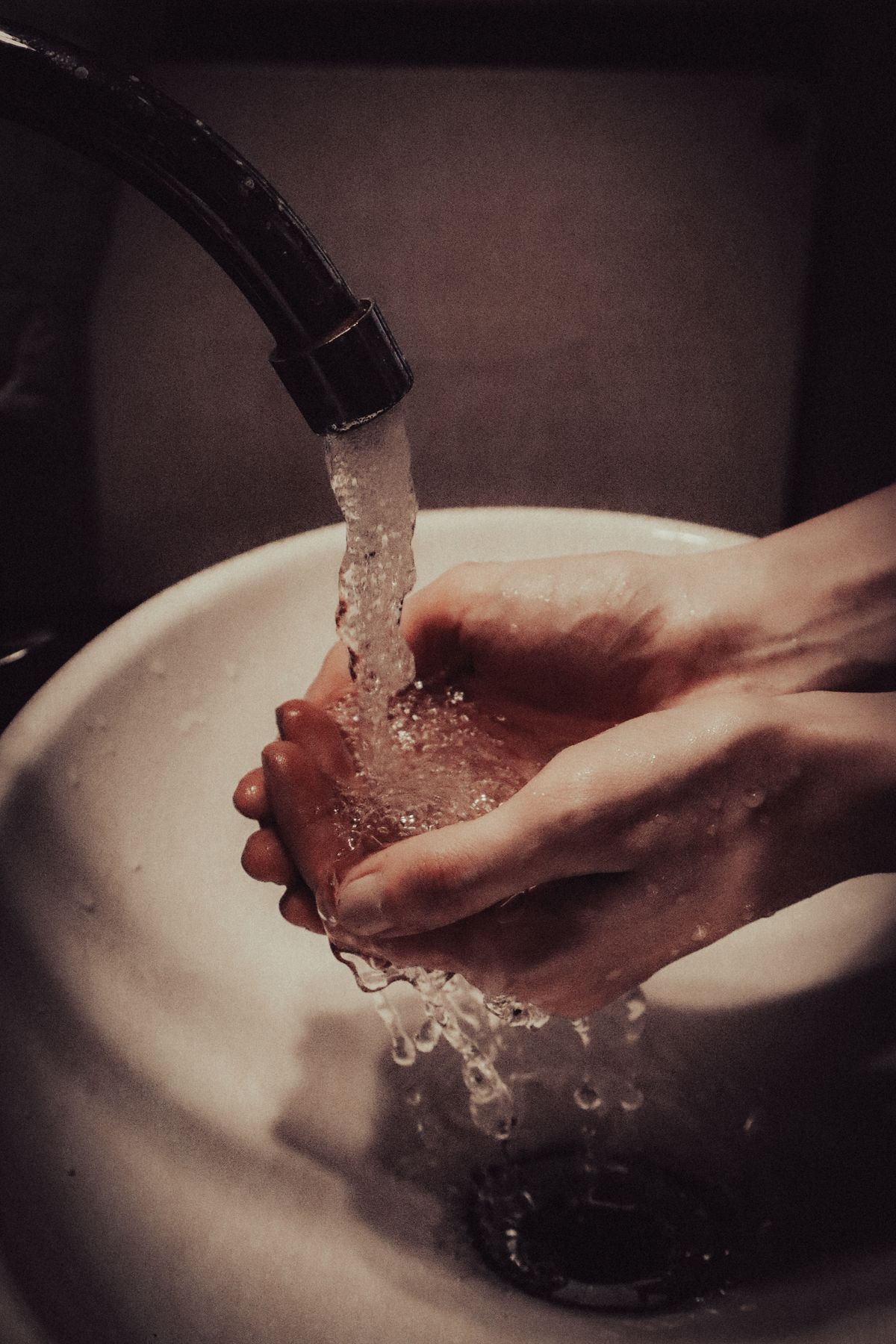 Hands cupped under a running bathroom faucet, rinsing in softened water that can feel slippery