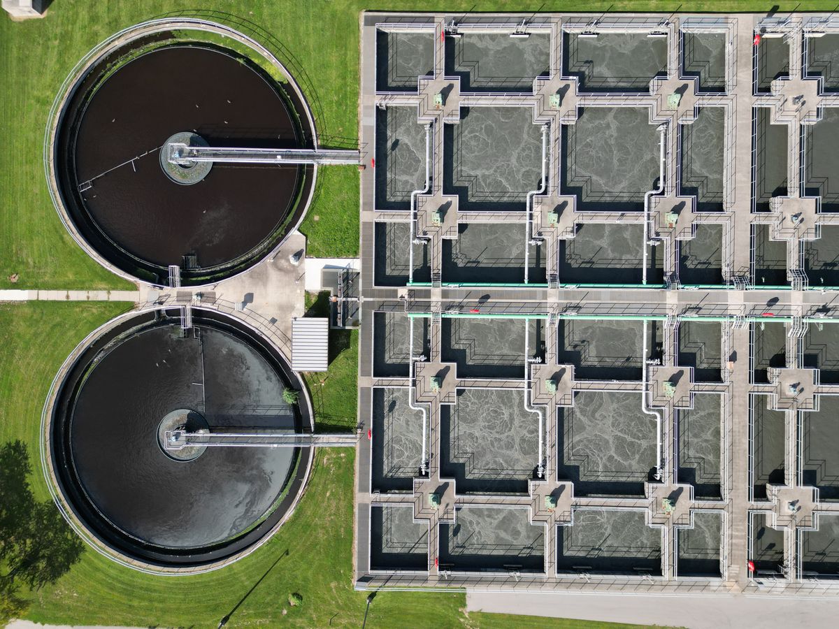 Aerial view of a municipal wastewater treatment plant with two round clarifiers beside a grid of rectangular aeration basins