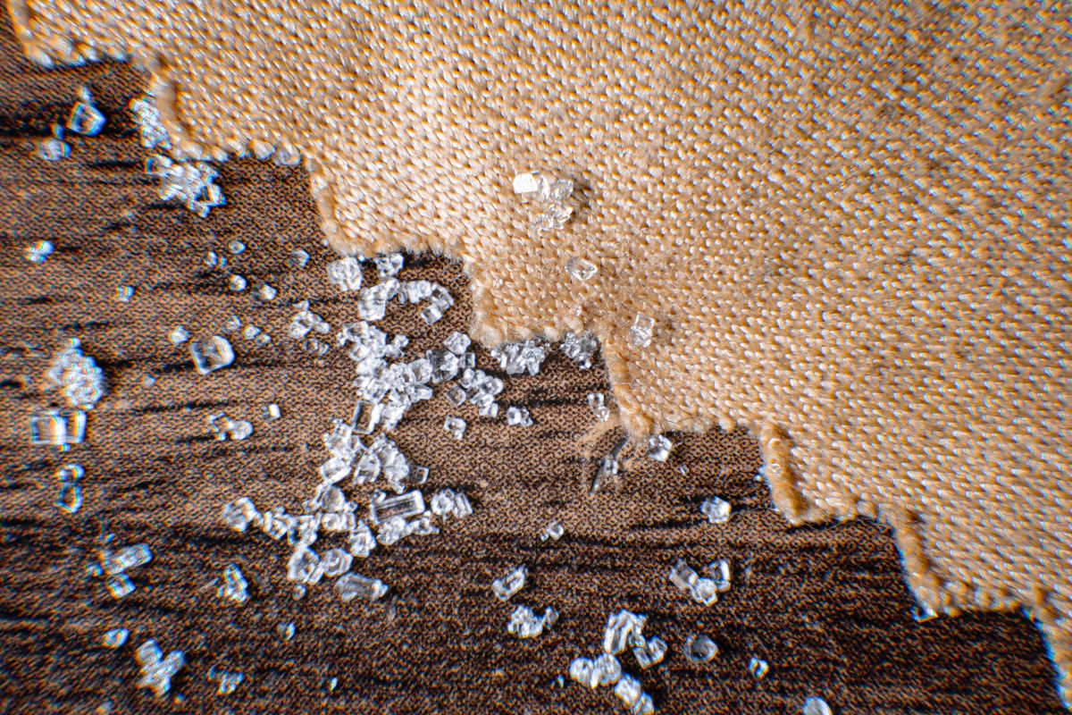 Macro close-up of clear cubic salt crystals scattered across burlap and dark wood
