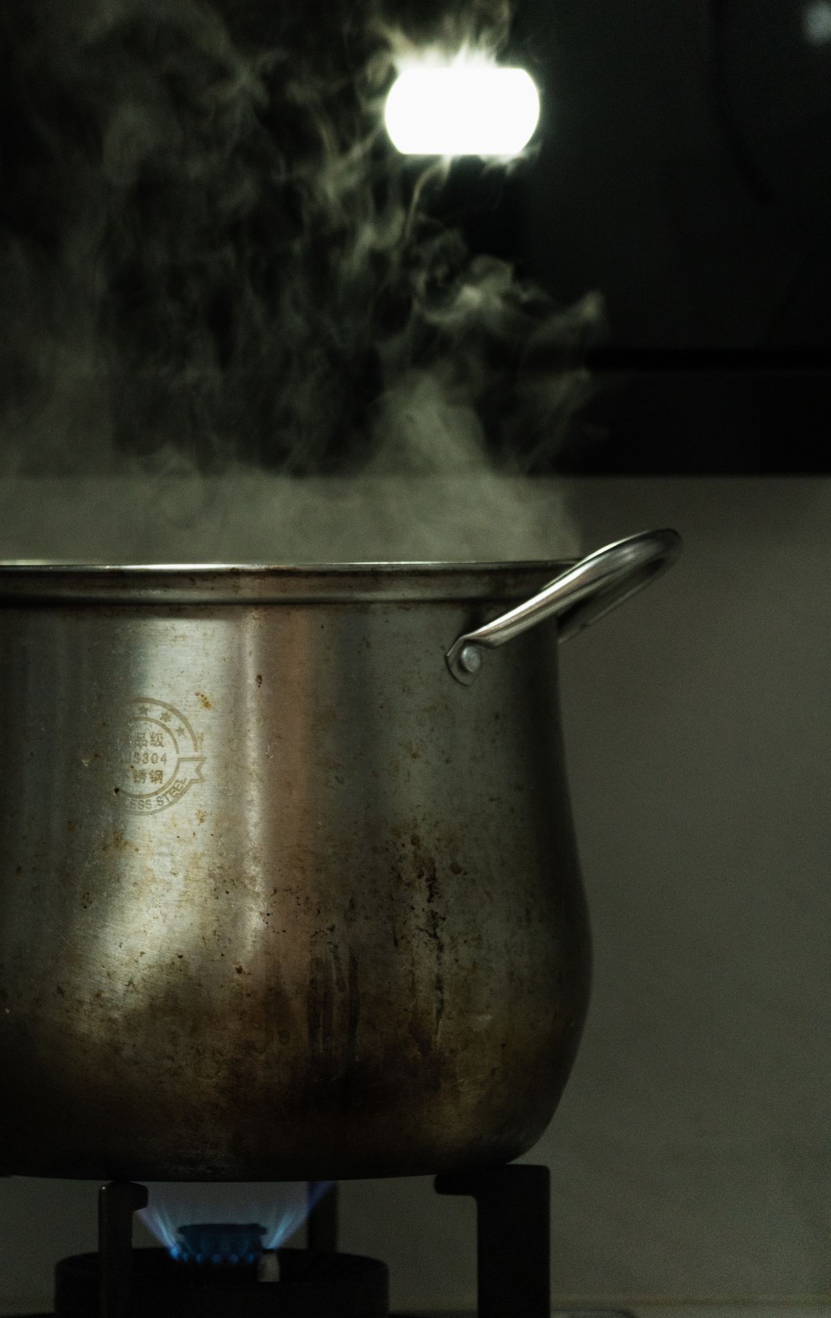 Stainless steel stock pot giving off steam as water boils on a gas stove burner
