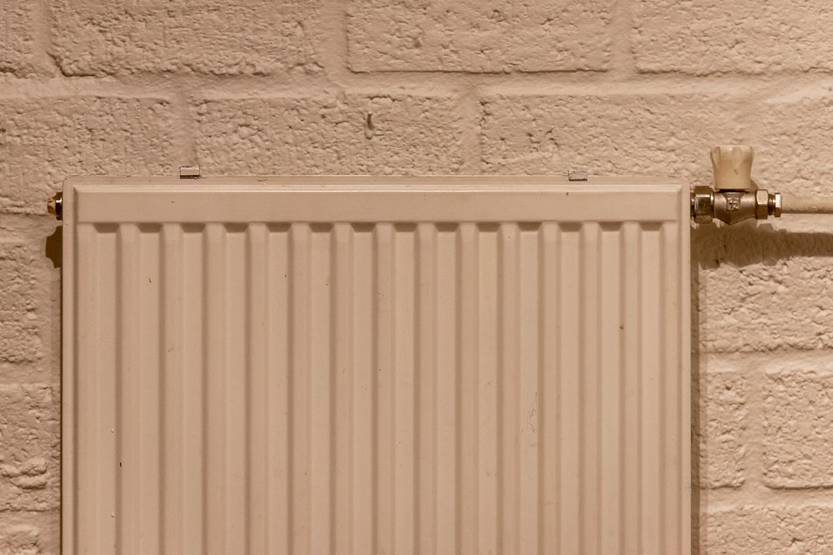 White panel radiator with a valve on a brick wall, part of a sealed hydronic loop that recirculates the same water