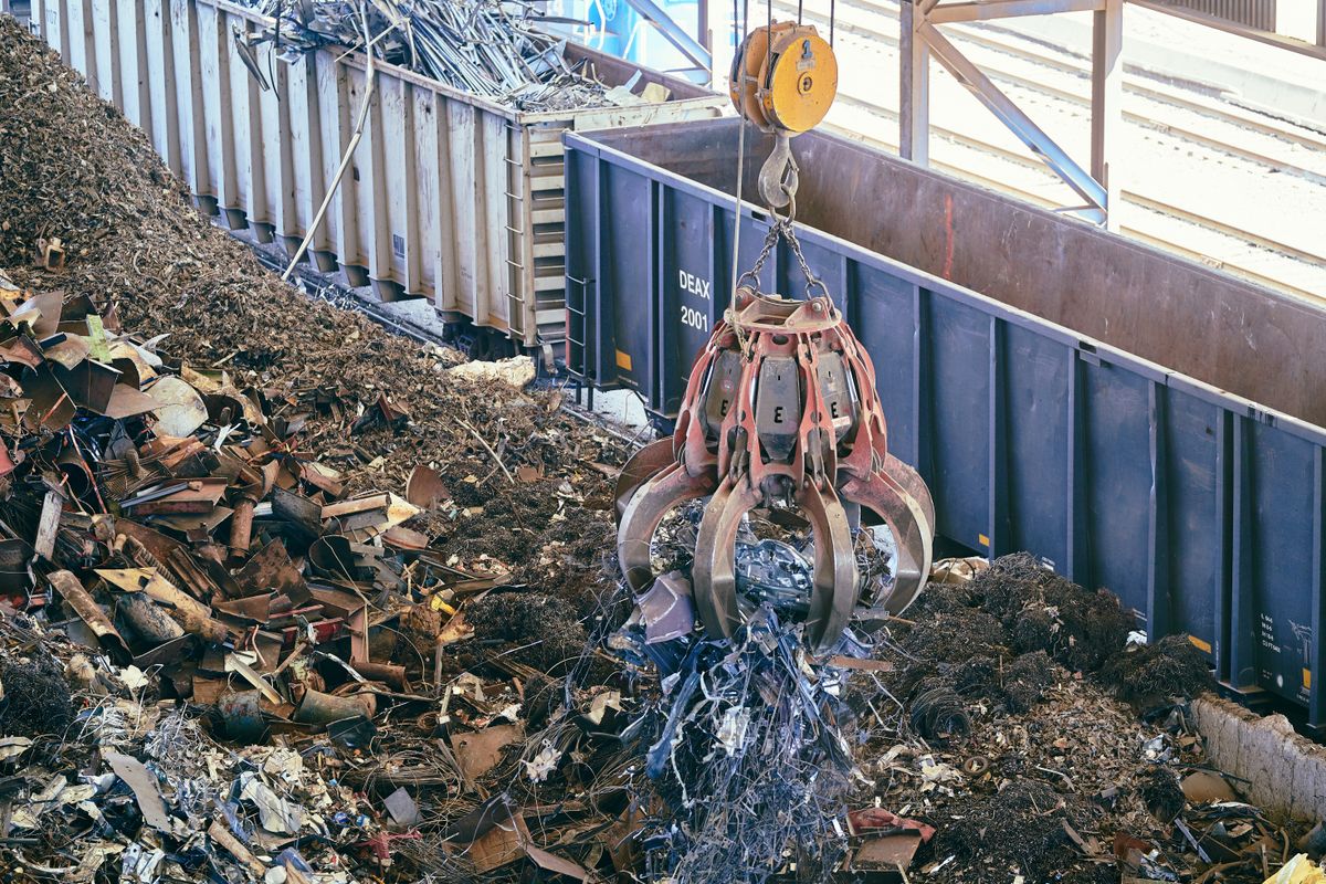 Grapple crane lifting shredded scrap metal into a rail car at a metal recycling yard