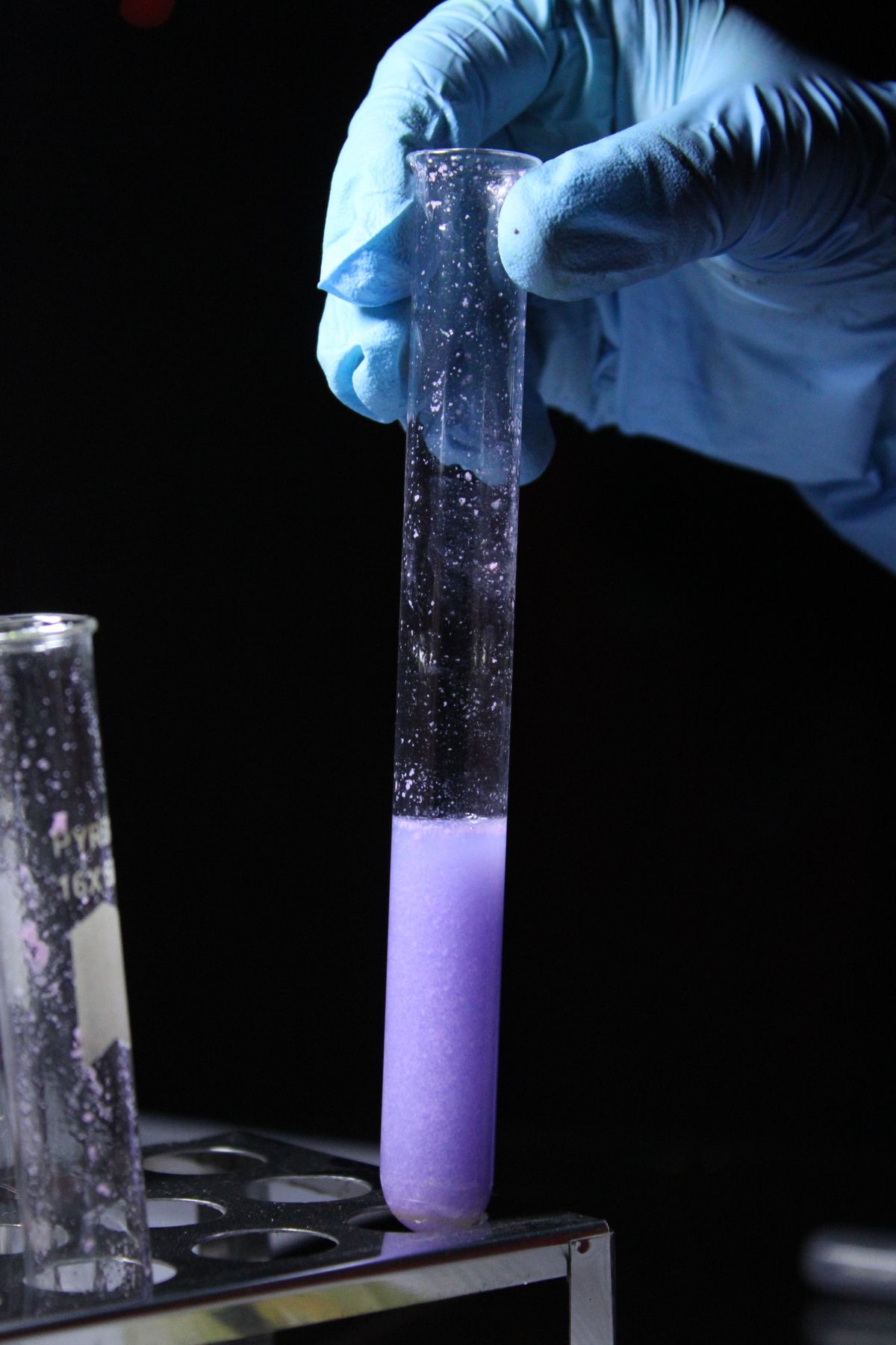 Gloved hand lifting a test tube of purple reagent from a rack during a water hardness test