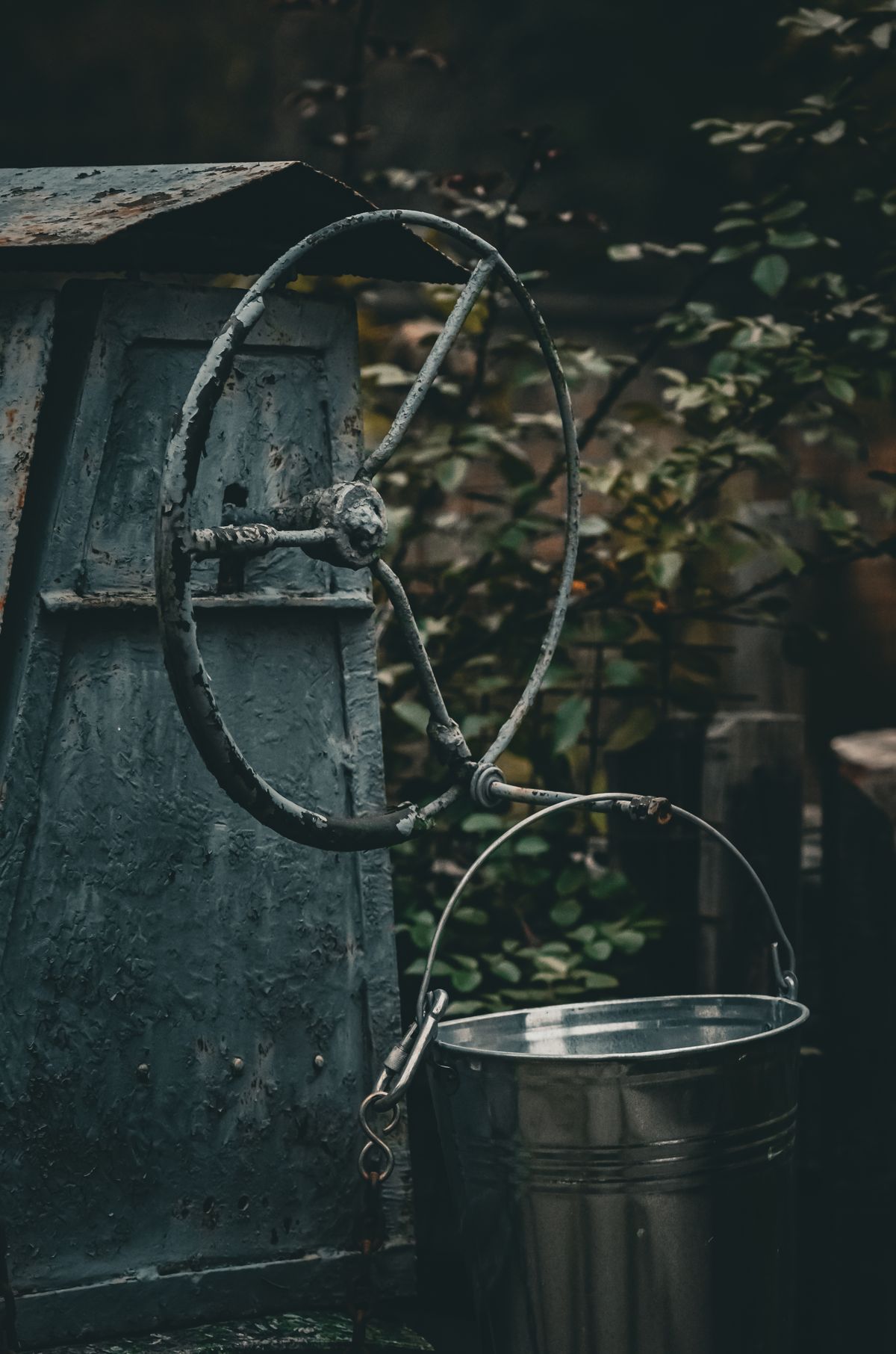 Weathered well housing with a rusting crank wheel and a galvanized bucket, the kind of private supply whose water carries both hardness and iron from the ground