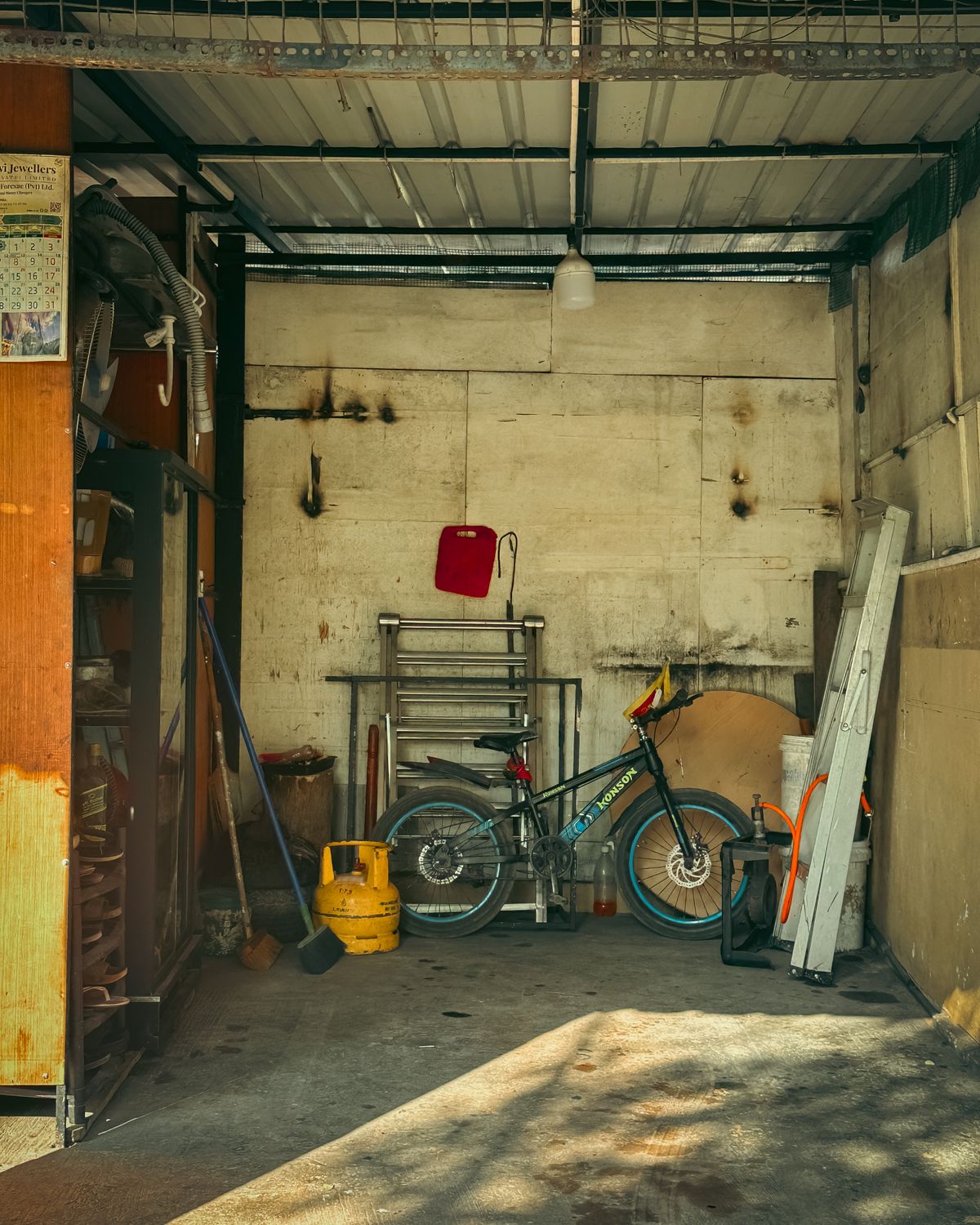 Unheated garage interior with a concrete floor, metal roof, bicycle, shelving and ladder, where a water softener would face winter freezing